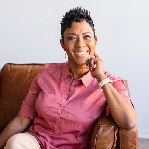 Black woman wearing a pink shirt sitting in brown leather chair